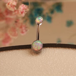 May include: A silver belly button ring with two round, iridescent opal stones. The stones display a mix of pink, green, and yellow hues. The curved bar connects the two opal stones, creating a simple yet elegant design.