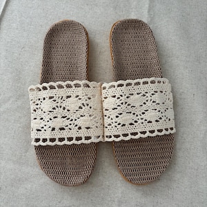 May include: A pair of brown and beige woven slippers with a cream-colored, crocheted band across the top. The slippers are designed for indoor wear and have a simple, elegant aesthetic.