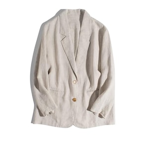 May include: A light beige blazer with a classic notched lapel and two front pockets. The blazer has a single-button closure and long sleeves. The fabric appears to be linen or a similar lightweight material, suitable for warmer weather.