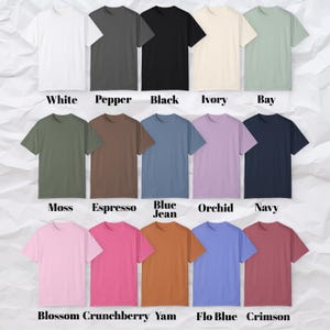 May include: A collection of short-sleeved t-shirts in various colors, including white, black, and blue. Each shirt has a crew neck and is displayed on a wrinkled white surface. The colors are labeled with text at the bottom.