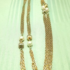 Puede incluir: Collar dorado con m&uacute;ltiples hilos, con peque&ntilde;as perlas y cuentas decorativas. El collar se muestra sobre un fondo verde claro texturizado, mostrando su delicado dise&ntilde;o y los intrincados detalles de la cadena.