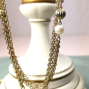Puede incluir: Un collar dorado con m&uacute;ltiples hilos, con una combinaci&oacute;n de eslabones de cadena, cuentas de metal acanaladas y acentos de perlas blancas. El collar se muestra sobre un fondo blanco.