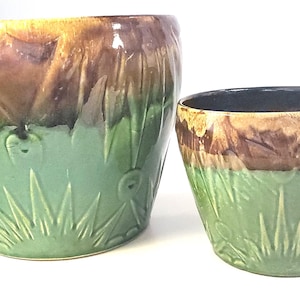 May include: Two ceramic plant pots with a glossy finish. The larger pot is brown and green, with a textured design. The smaller pot is also brown and green. Both pots have a unique, decorative style.