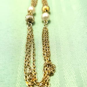 Puede incluir: Un collar dorado con dise&ntilde;o de cadena, con perlas y detalles de cuentas texturizadas. El collar tiene dos borlas de cadena. El fondo es de tela verde claro.