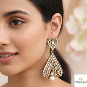 May include: Gold-toned, heart-shaped and teardrop-shaped earrings with clear, round and pear-shaped crystals. The earrings have a pearl at the bottom and are worn on the ear. The earrings are part of the Fancy Fab Jewels collection.
