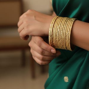 May include: A set of gold bangles with a textured surface. The bangles are stacked on a wrist, with a green fabric in the background.