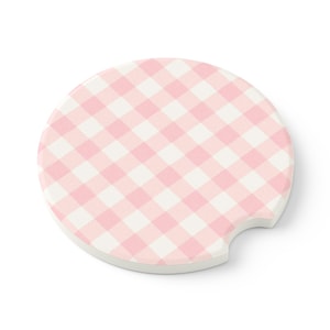 May include: Pink and white gingham patterned coaster. The coaster is round with a cutout for a beverage.