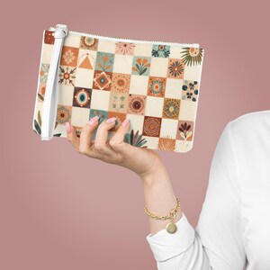 May include: A cream-colored clutch with a colorful patchwork design featuring floral and geometric patterns in shades of orange, teal, and brown. The clutch has a white wrist strap and a zipper closure.