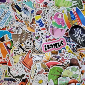 Puede incluir: Una gran colección de pegatinas de vinilo variadas con diversos diseños coloridos, incluyendo un flamenco rosa, un perezoso, una margarita, el Coliseo, tablas de surf y elementos de texto como 'yikes!' y 'made in the air' esparcidos.