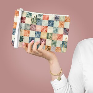 Op de afbeelding: Een rechthoekige clutch met een witte polsband. De clutch heeft een patchwork-ontwerp van vierkanten in verschillende kleuren, waaronder oranje, blauw en groen, elk versierd met botanische illustraties. De rits is wit.