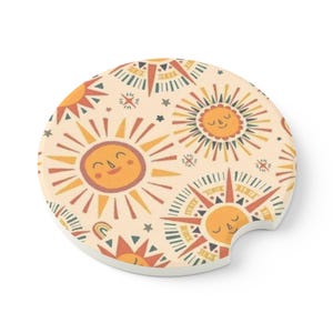 May include: Round coaster with a repeating pattern of smiling suns with orange, yellow, red, and green rays. The background is a light cream color with small stars.