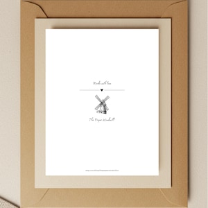 Op de afbeelding: Een witte kaart met een zwarte illustratie van een windmolen, de tekst "Made with love" en "The Paper Windmill" in een bruine envelop. De kaart heeft een hartsymbool boven de windmolenillustratie.