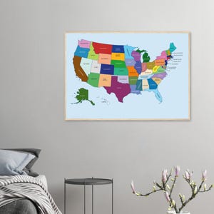 May include: A framed map of the United States, showcasing each state in a different color. The map is set against a light blue background and is enclosed in a wooden frame. The states are labeled with their names in a clear font.