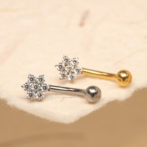 Puede incluir: Dos pendientes de cartílago con forma de flor. Un pendiente tiene un poste plateado y un extremo de bola plateada, y el otro tiene un poste dorado y un extremo de bola dorada. Las partes superiores en forma de flor están incrustadas con pequeños cristales transparentes.