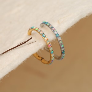 May include: Two silver and gold rings with a row of iridescent opal stones. The rings are on a white background.