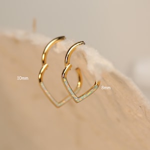 May include: A pair of gold heart-shaped hoop earrings with white opal accents. The earrings are available in two sizes: 10mm and 8mm.