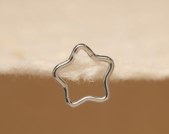 May include: A silver-colored, star-shaped earring or body jewelry. The five-pointed star has a smooth, polished finish and a hinged clasp. The jewelry is set against a soft, off-white background.