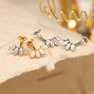 Könnte beinhalten: Drei Schmuckstücke werden gezeigt. Zwei sind goldfarben und eines silberfarben. Jedes Stück hat ein fächerförmiges Design mit mehreren klaren und weißen Edelsteinen. Bei dem Schmuck handelt es sich wahrscheinlich um Ohrringe oder Körperschmuck.