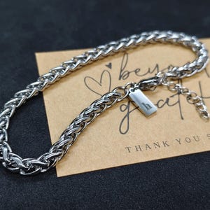 May include: A silver chain bracelet with a woven pattern. The bracelet features a small rectangular tag with the letter "h". The bracelet is displayed on a brown card with the words "beyond grateful" and "THANK YOU so much".
