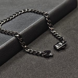 May include: A black chain bracelet with a black metal clasp. The clasp has the letters "K&B" engraved on it.