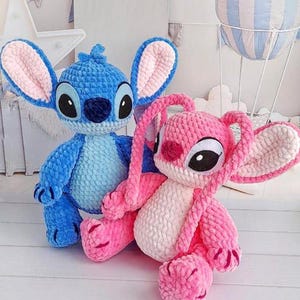 May include: Two handmade crochet plush toys. One is blue with large ears and black eyes, the other is pink with similar features. Both have a soft, textured appearance. The toys are likely inspired by a popular animated character.