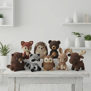 Puede incluir: Una colección de ocho pequeñas figuras de animales del bosque tejidas a ganchillo, que incluyen un castor marrón, un zorro rojo, un mapache gris, un erizo beige, un búho marrón, un oso oscuro, un conejo beige y un alce con grandes astas.