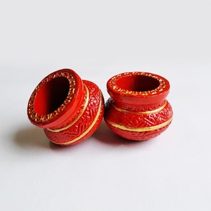 May include: Two small, round, red pots with open tops. Each pot features a wide, gold-painted rim with a repeating circular pattern and a horizontal gold band around the center. The exterior surface is decorated with embossed geometric patterns.