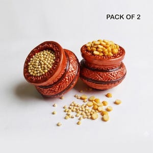 May include: Two terracotta-colored pots with intricate carved designs. One pot is open, filled with small, round, light-colored seeds. The other pot is filled with yellow split peas. The text "PACK OF 2" is visible.