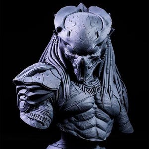 May include: A detailed gray and black Predator bust sculpture with a textured surface and intricate details. The bust features a detailed head with a mask and dreadlocks.