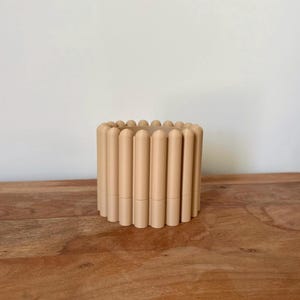 May include: A small, beige ceramic planter with a unique ribbed design. The planter is labeled "Size Small" and "Color Mocca Mousse".