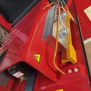 May include: A red metal machine with a yellow warning sign and a black and white warning sign that says "Ghost Trap". The machine has a silver heat sink with wires attached to it.