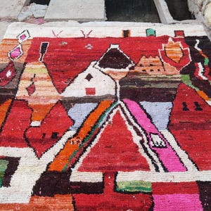 May include: A colorful rug with a geometric design featuring red, orange, pink, white, and brown hues. The rug has a hand-woven texture and a unique abstract pattern.