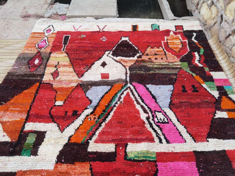 May include: A colorful rug with a geometric design featuring red, orange, pink, white, and brown hues. The rug has a hand-woven texture and a unique abstract pattern.