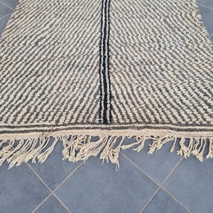May include: A black and white striped rug with a fringe border. The rug has a subtle wave pattern and a black stripe down the center.