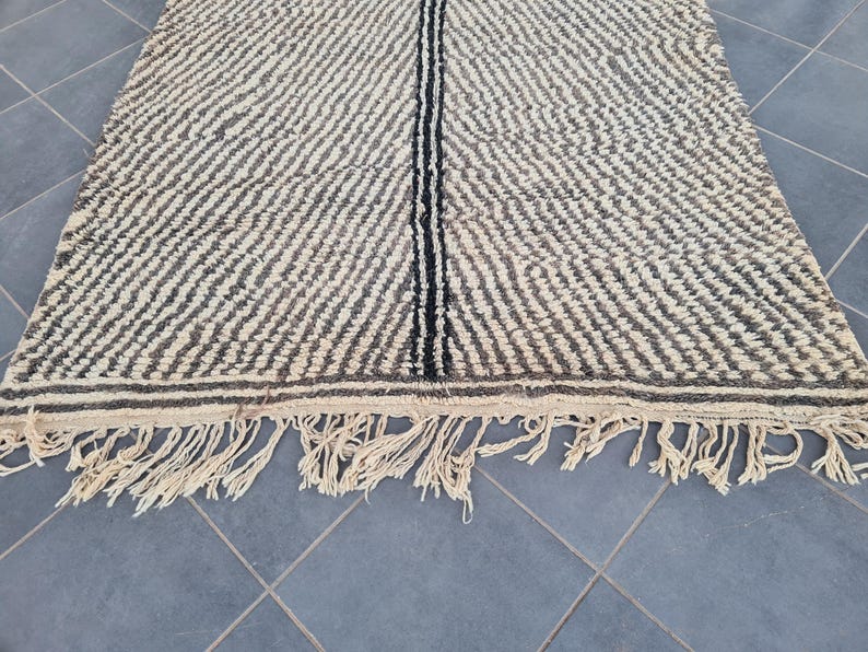 May include: A black and white striped rug with a fringe border. The rug has a subtle wave pattern and a black stripe down the center.