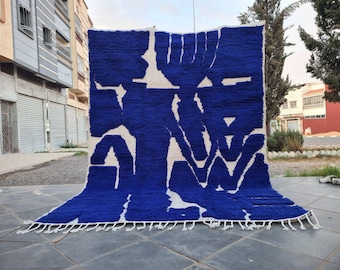 May include: A large, rectangular rug with a bold blue and white abstract design. The rug features a thick, textured pile and a fringe along the bottom edge. The color palette is a striking contrast of deep blue and off-white.