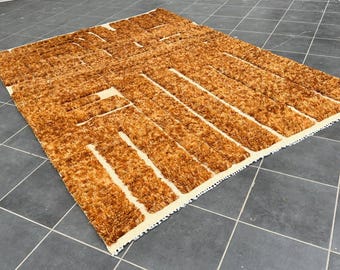May include: A rectangular rug with a textured, shaggy pile in shades of brown and beige. The rug features a geometric pattern of parallel lines and rectangular shapes. The rug is placed on a gray tiled floor.
