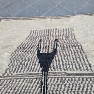 May include: A white rug with a black geometric design. The design features a large, abstract shape in the center of the rug.