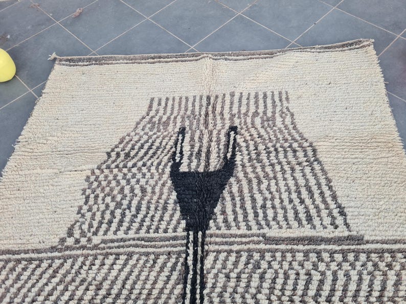 May include: A white rug with a black geometric design. The design features a large, abstract shape in the center of the rug.