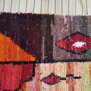 May include: A colorful, abstract rug with a geometric pattern in shades of orange, red, brown, and white. The rug is made of a thick, textured material and has a hand-woven look.