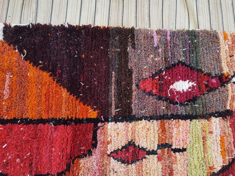 May include: A colorful, abstract rug with a geometric pattern in shades of orange, red, brown, and white. The rug is made of a thick, textured material and has a hand-woven look.
