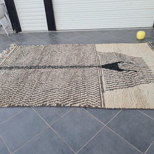 May include: A black and white patterned rug with a geometric design. The rug is made of natural fibers and has a fringed edge.