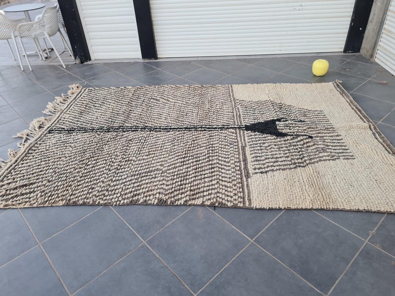 May include: A black and white patterned rug with a geometric design. The rug is made of natural fibers and has a fringed edge.