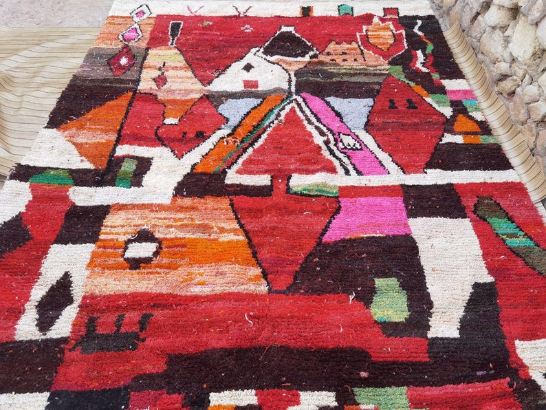 May include: A colorful Moroccan rug with geometric patterns in shades of red, orange, white, black, and green. The rug features a central diamond shape with smaller geometric shapes surrounding it.