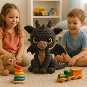 May include: A dark grey crocheted dragon toy with large yellow eyes and small black wings. The dragon is sitting on a light-coloured carpet, with a teddy bear, a wooden stacking toy, and a wooden train nearby. Two children are smiling in the background.