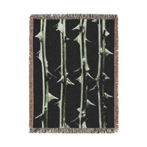 Op de afbeelding: Een zwart en groen geweven deken met een patroon van doornige takken.