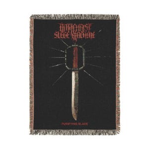 May include: Black woven throw blanket with a red and white design. The design features the text "Antichrist Siege Machine" above a stylized sword and the text "Purifying Blade" below. The blanket has a fringed edge.