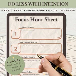 May include: A digital planner with the text "Focus Hour Sheet" and "3 Pages Declutter, Focus & Reset." A hand holds a pen over the planner. A cup of coffee and other planning sheets are also visible.