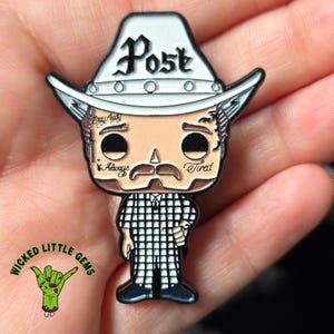 May include: A novelty pin featuring a cartoon-style figure with a cowboy hat that reads "Post". The figure has tattoos that say "Stay Away", "Always", and "Tired". The figure is wearing a black and white checkered shirt.