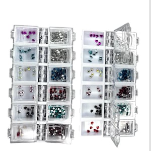 May include: A clear plastic storage box with 14 compartments for storing small items. Each compartment is filled with colorful rhinestones. The box is open to reveal the contents.